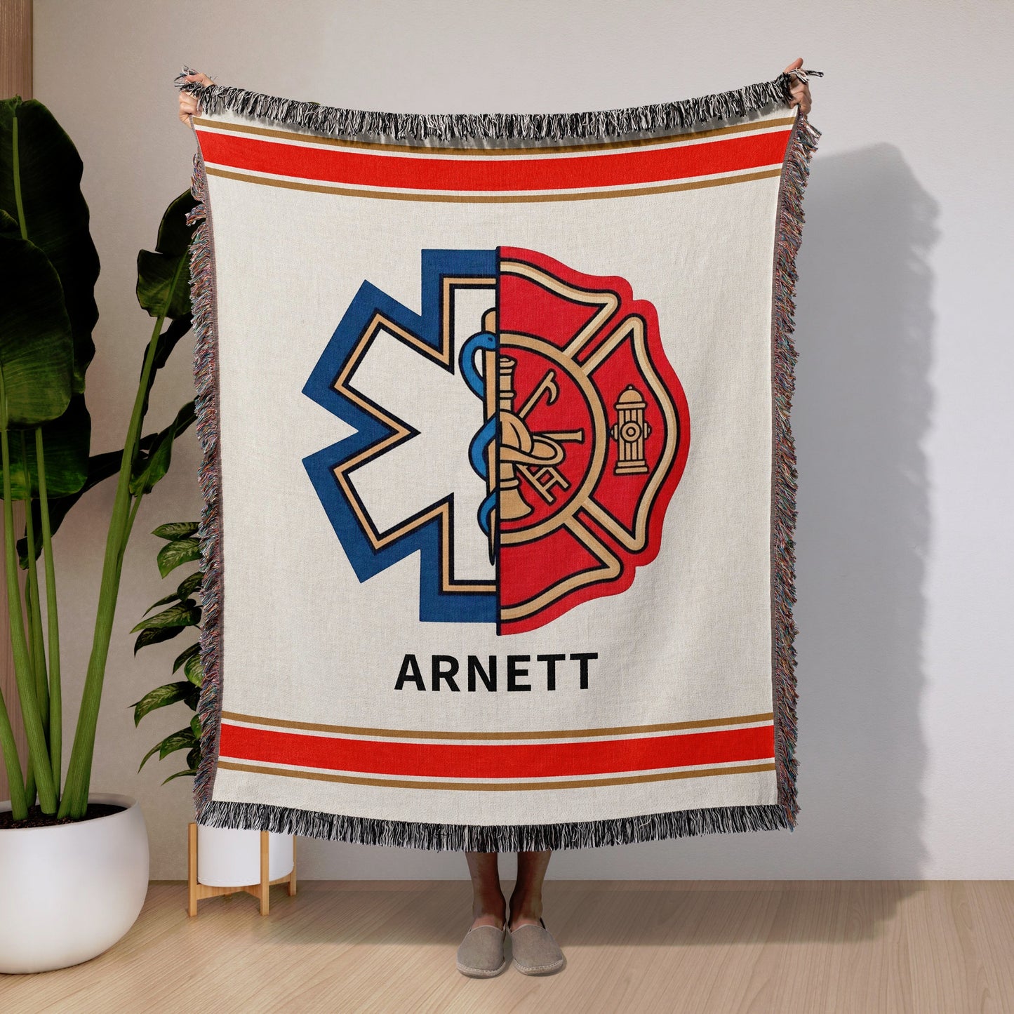 Firefighter Paramedic EMT Woven Blanket with a logo and name text held by a person in a room with a plant and wooden floor.